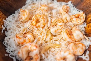 Macro closeup of homemade basmati rice, cooked whole large king jumbo Argentinian fried shrimp seafood with sweet onion slices on wooden plate