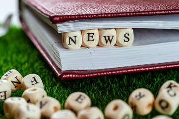 The word news is made of wooden cubes, between the pages of a notebook.