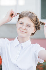 The concept of education. Girl pupil of elementary school in glasses in uniform fooling around with pigtails and smile. Funny girl in glasses ready for school.