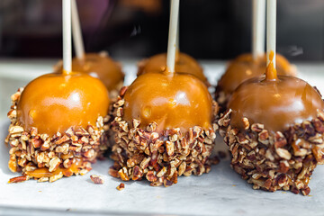 Caramel caramelized apples with pecan nuts on sticks sweet candied food dessert on retail display...