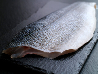 A fillet of fresh raw sea bass on a black slate plate, black isolated background 