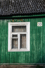 Fototapeta na wymiar a part of an old green wooden house with white window frame and house number 33