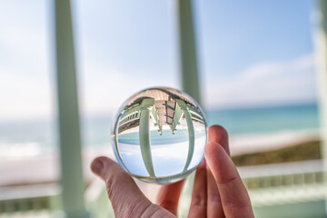 Seaside, Florida with hand holding lensball crystal glass ball with reflection of green wooden pavilion gazebo architecture by beach ocean in blurry background view