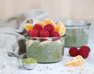 A healthy Chia pudding Matcha kn green tea, chia seed know as a super food, with sliced banana, raspberries and orange in jar on wooden table 