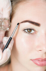 Young woman correcting eyebrow shape with brush, closeup