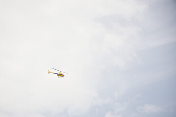 Isolated yellow helicopter flying through the sky. Weather is slightly cloudy.