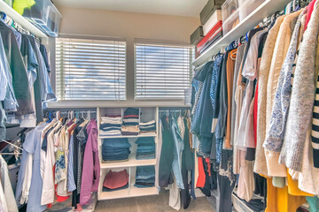 Walk in closet interior with hanging clothes and a view of a cloudy sky through the windows
