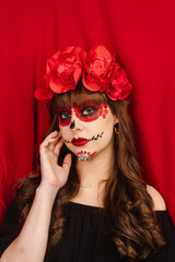 Portrait of a beautiful girl with Dia de los Muertos makeup with red background.