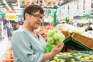 An elderly woman in chooses apples in the store. Grandma in the fruit section of the supermarket.