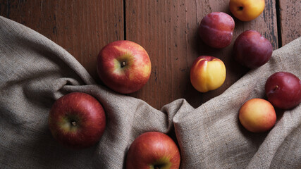 Juicy fruits in a linen tablecloth on a old wooden table. Apples, plums, apricots on a dark red background