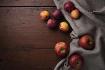 Fruits in a linen tablecloth on a old wooden table. Apples, plums, apricots on a dark red background