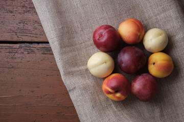 Juicy fruits in a linen tablecloth on a old wooden table. Plums, apricots on a dark red background