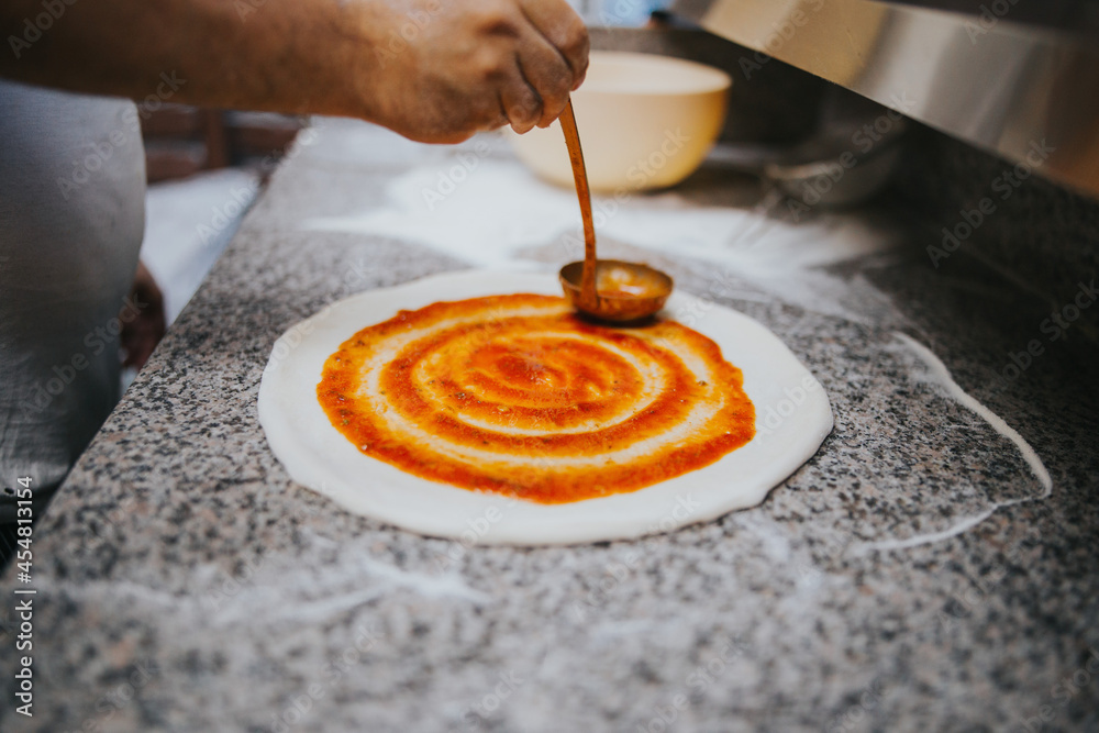 Sticker chief spreading tomato sauce over the pizza dough to make pizza margherita