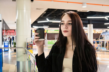 Beautiful girl drinks coffee in the shopping center.