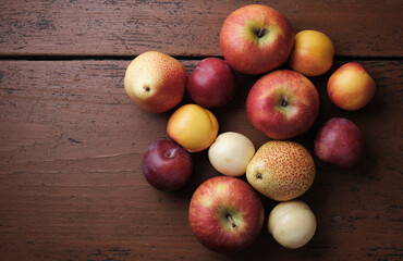 Juicy fruits on a old wooden table. Apples, pears, plums, apricots on a dark red background