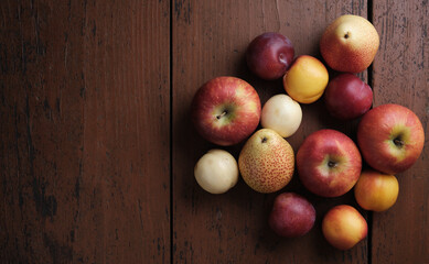 Autumn fruit on a wooden table. Apples, pears, plums, apricots on a dark red background