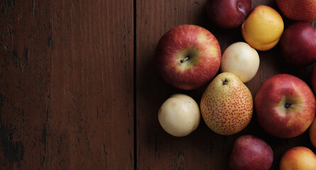 Fruits on a old wooden table. Apples, pears, plums, apricots on a dark red background