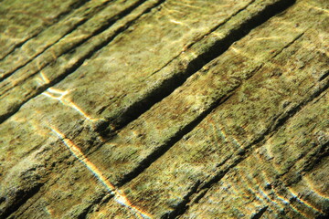 水面の波形が光に照らされて映っている、水中の岩の表面