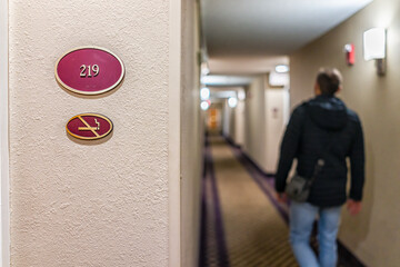 Closeup of sign at inn hotel motel with number for non-smoking room and man traveler walking at...