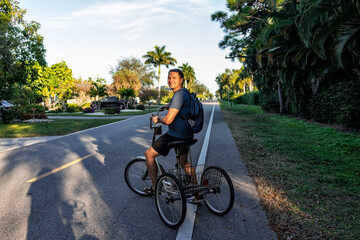 One young man standing riding tricycle bike with backpack on road at Naples park residential...
