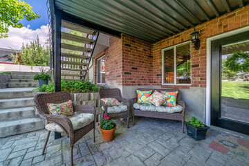Woven couch and armchairs on an outdoor patio under the deck of a house with bricks
