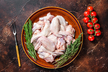 Cut Raw chicken wings in a rustic plate with thyme and rosemary. Dark background. Top view