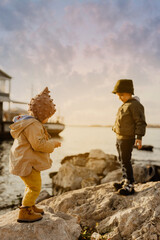 a boy and a girl are standing on the rocks on the seashore at sunset
