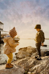 Fototapeta premium a boy and a girl are standing on the rocks on the seashore at sunset
