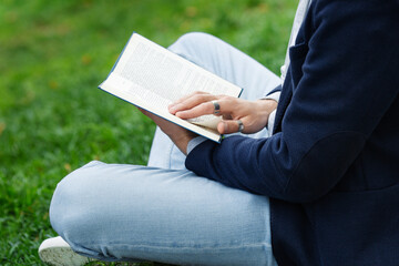 Man reading book in park. Cropped image of casual writer guy, psychologist or student prepare for exam in university with educational literature outside. Reader chilling with bestseller on green grass