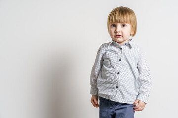 Half length portrait of small blonde caucasian boy standing in front of white wall looking to the side - little child studio portrait with copy space