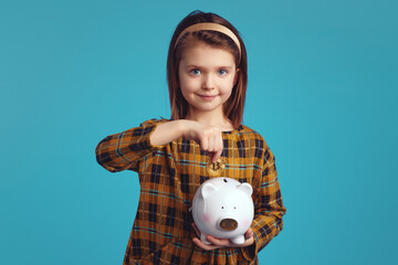 Fototapeta na wymiar Little charming girl kid holding piggy bank and putting bitcoin coin in it, isolate over blue studio background