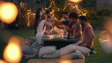 young group of friends celebrating at dinner party chatting sharing healthy food sitting at table enjoying weekend reunion relaxing on beautiful summer evening outdoors 4k