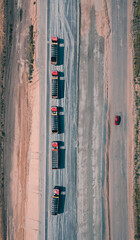 Convoy of trucks rides on asphalt road with one red car on another side of road, top view. Trucks carry building materials for construction of the road. Top drone shot.