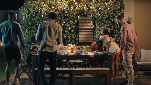 happy friends arriving at dinner party celebration hugging enjoying friendship reunion gathering sitting at table with healthy food sharing weekend together on beautiful summer night 4k