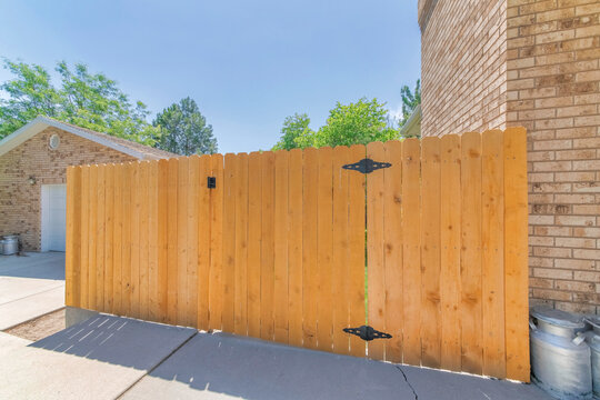Wooden hinged gate of a backyard of a house with brown bricks