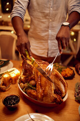 Close-up of black man carves turkey meat during Thanksgiving meat at dining table.