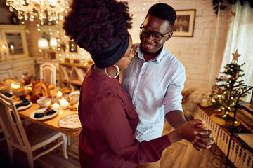 Young happy black couple enjoys while dancing in dining room on Thanksgiving.