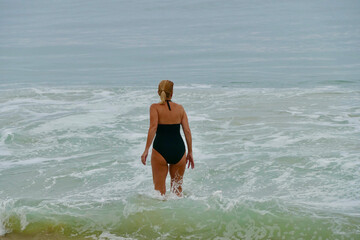 woman in black swimsuit wading into ocean