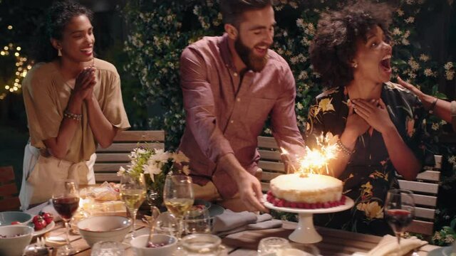 friends celebrating birthday party dinner surprising friend with cake happy woman laughing enjoying fun evening celebration on beautiful summer night at home 4k