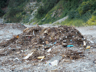 A pile of garbage brought from the sea on a pebble shore near a green hillock