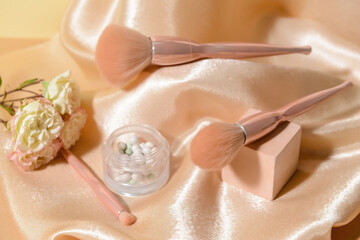 Makeup brushes with powder and decor on fabric background