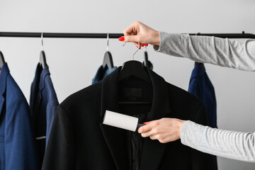 Woman cleaning jacket with lint roller on light background