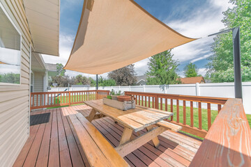 Deck of a house with wooden chairs and table under a shade sail - obrazy, fototapety, plakaty
