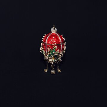 Traditional russian souvenir in Faberge style, enamel red gilded egg on black background jewelled precious crystals and pearls, replica of famous Lilies of Valley Faberge egg in Art Nouveau style