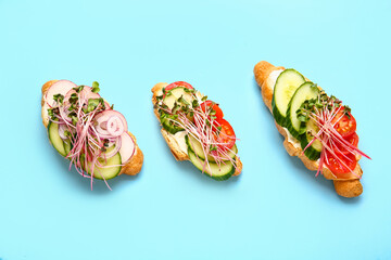 Tasty croissants with vegetables and micro green on color background