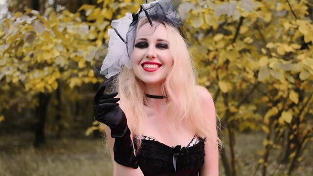A beautiful girl in the image of a witch in black gloves with black eyes and red lips. Smiles playfully
Halloween, autumn holiday concept. Slow motion, 4k footage 