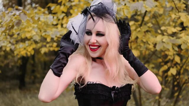 A beautiful girl in the image of a witch in black gloves with black eyes and red lips. Smiles playfully.
Halloween, autumn holiday concept. Slow motion, 4k footage