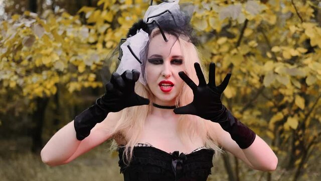 A beautiful girl in the image of a witch with black eyes and red lips. With black gloves. Scares and beckons.
Halloween, autumn holiday concept. Slow motion, 4k footage 