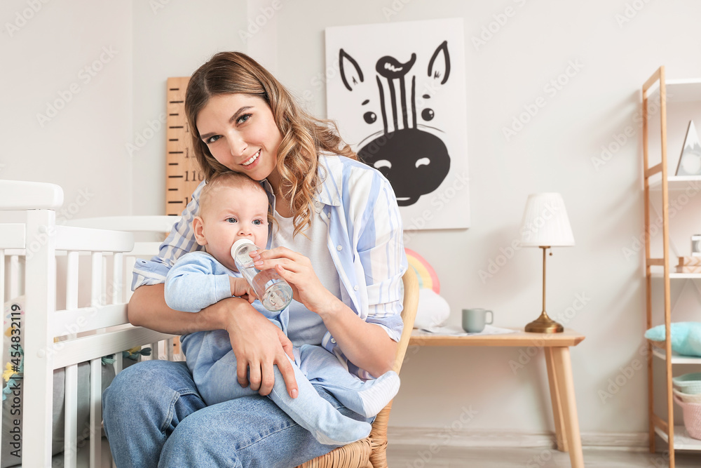 Wall mural Young mother giving water to her cute baby at home