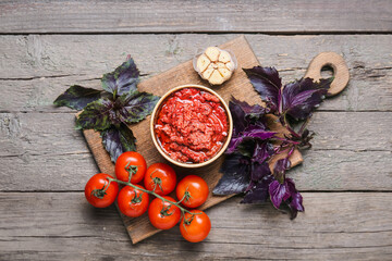 Board with bowl of tasty pesto sauce and ingredients on wooden background